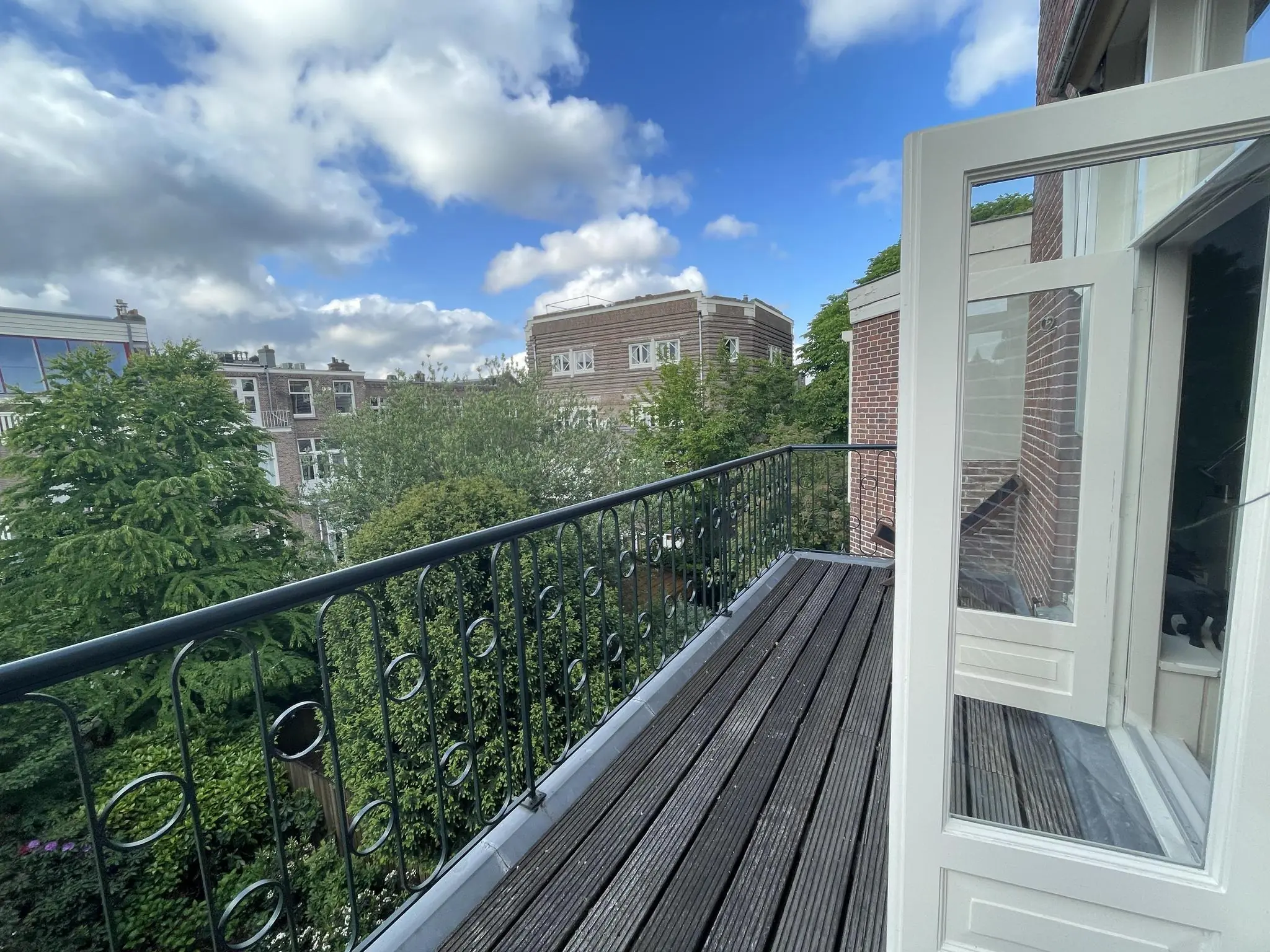 Balkon aan de Oranje Nassaulaan met uitzicht op groene bomen en omliggende bakstenen gebouwen onder een deels bewolkte lucht.